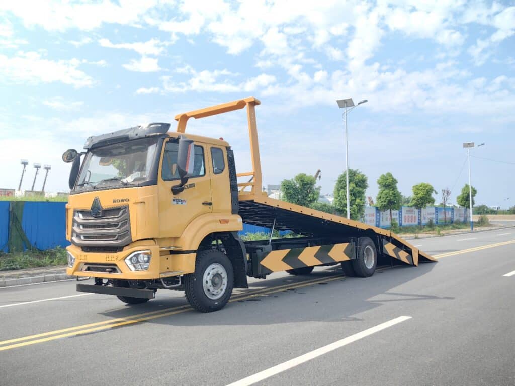 Left Front 45-Degree View of SINOTRUK Flatbed Tow Truck with Close-Up of Hydraulic Flatbed Lift